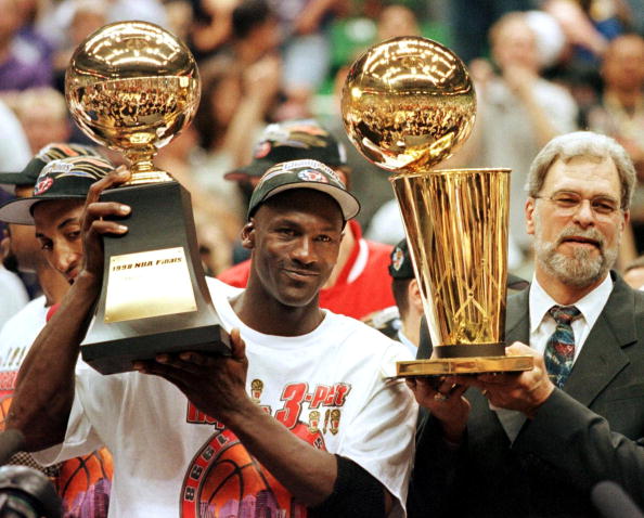 SALT LAKE CITY, UNITED STATES:  In this 14 June 1998 file photo, Michael Jordan (L) holds the NBA Finals Most Valuable Player trophy and former Chicago Bulls head coach Phil Jackson holds the NBA champions Larry O'Brian trophy 14 June after winning game six of the NBA Finals with the Utah Jazz at the Delta Center in Salt Lake City, UT. The Bulls won the game 87-86 to take their sixth NBA championship. Jackson left the Bulls following the 1998 season and 12 January reports indicate that Jordan plans to announce his retirement at a 13 January news conference in Chicago.   AFP PHOTO/FILES/Jeff HAYNES (Photo credit should read JEFF HAYNES/AFP via Getty Images)