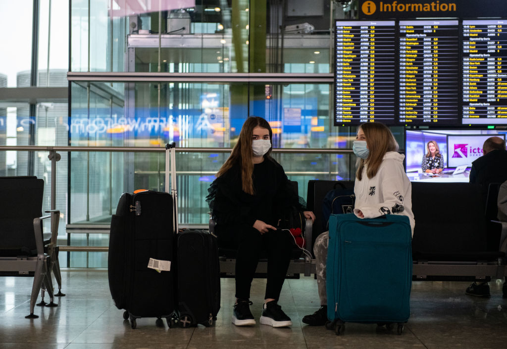 LONDON, ENGLAND - MARCH 15: Airline passengers wearing face masks sit with their bags at departures at Heathrow Terminal 5  as the outbreak of coronavirus intensifies on March 15, 2020 in London, England. President of the United States, Donald Trump, has implemented a travel ban on European nations and has now extended it to include the United Kingdom and Ireland. The travel ban will begin at midnight EST on Monday as the UK is also set to ban mass gatherings and has already seen the cancellation of major sporting events such as the English Premier League. (Photo by Chris J Ratcliffe/Getty Images)
