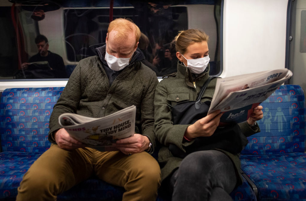 LONDON, ENGLAND - MARCH 19: A couple sit on the Central Line Tube wearing protective face masks while reading a newspaper on March 19, 2020 in London, England. Transport for London announced the closure of up to 40 stations as officials advised against non-essential travel. Bus and London Overground service will also be reduced. (Photo by Justin Setterfield/Getty Images)