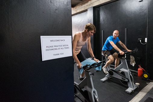 Gym reopening with enhanced COVID policies. Reopening after a pandemic. Two people train on exercise bikes at the gym
