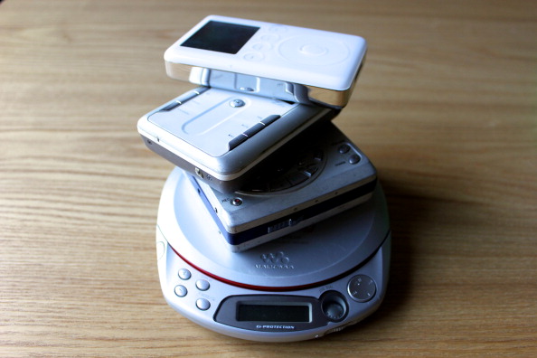 Stack of old music devices; Sony Atrac3Plus Car Ready CD Walkman,  Sharp MD-MT161 MiniDisc Portable Recorder, Creative Zen DAP-HD0014 MP3 Player and Apple iPod 3rd Generation MP3 Player.