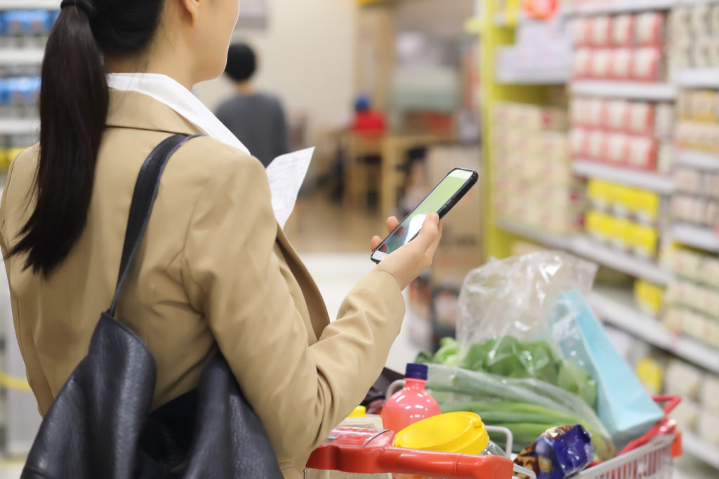 Woman holding shopping list with smartphone in supermarket