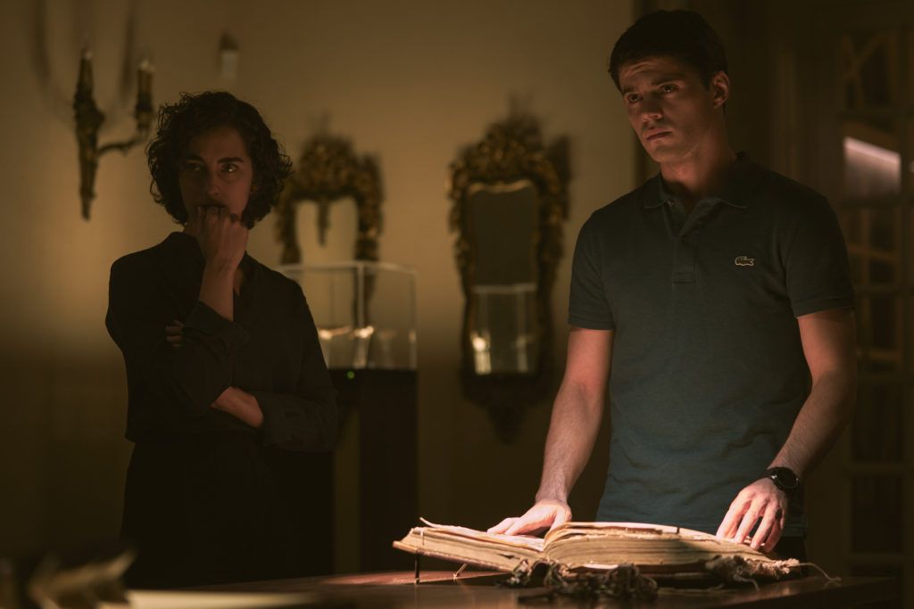 Javier Morgade as Martin flicks through ancient book with Maria Caballero as Diana by his side seen in The Girl in the Mirror