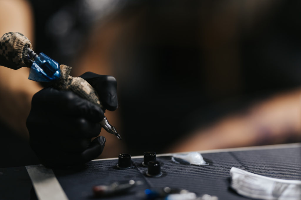 Tattoo master dips a tattoo machine with needles in black ink