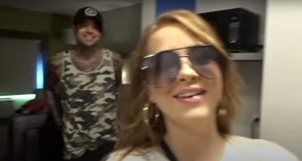 Ashlyn Vanhorn wearing sunglasses and large earrings with Jon Hill behind her wearing a black cap, inside a cruise ship bedroom