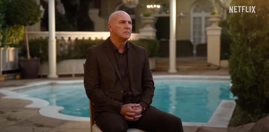 Arnold Vosloo as Daan Ludik sits beside a pool with his hands folded in Netflix's Ludik
