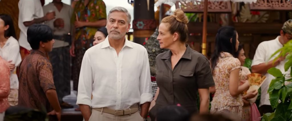 Julia Roberts looks at George Clooney in a busy Bali market as she reaches into her pocket in Ticket to Paradise