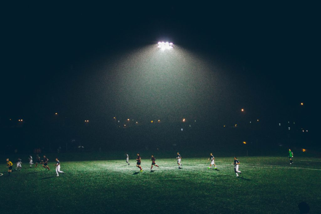 Soccer players play on a pitch at night under floodlights