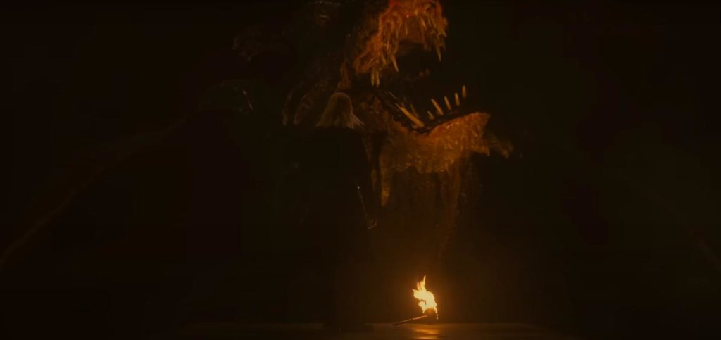 Daemon se para frente a un dragón a la luz del fuego mientras el dragón muestra sus dientes