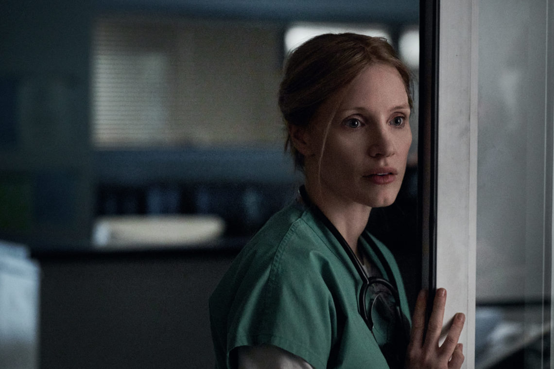 Jessica Chastain as Amy Loughren stands in scrubs leaning on hospital room doorway