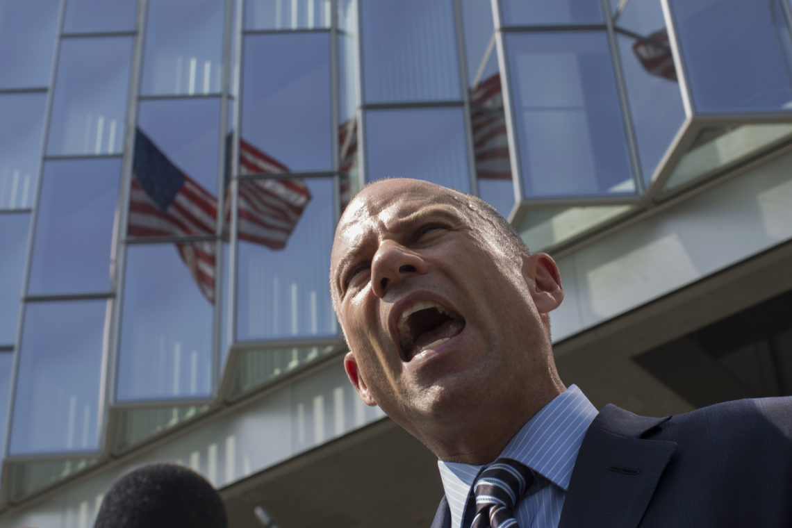 Michael Avenatti pictured from below, with US flags behind him, in animated speech