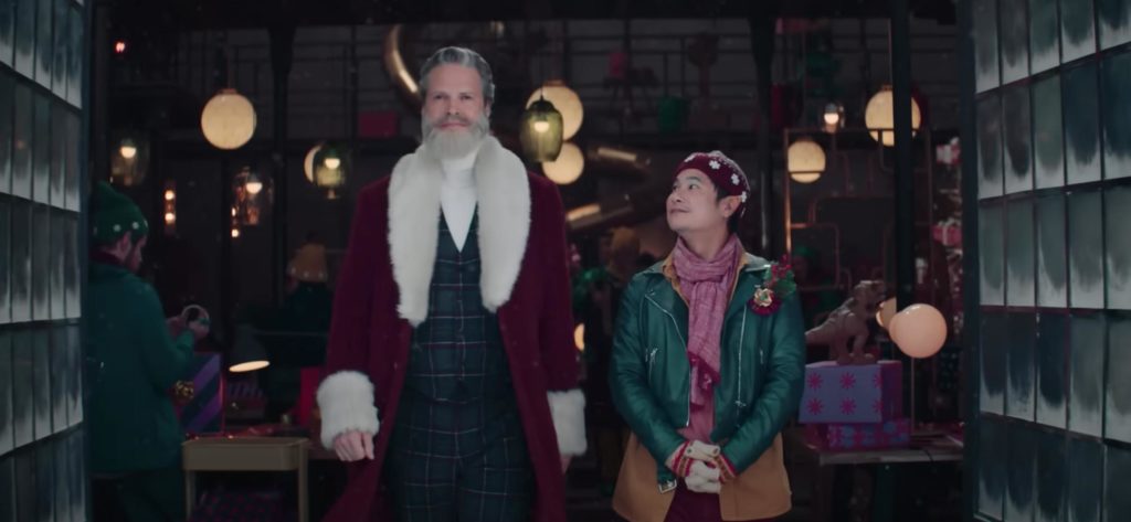 James Kirkland as Santa Claus in Rakuten's Christmas 2022 TV commercial, stepping outside his elves' workshop with one elf beside him