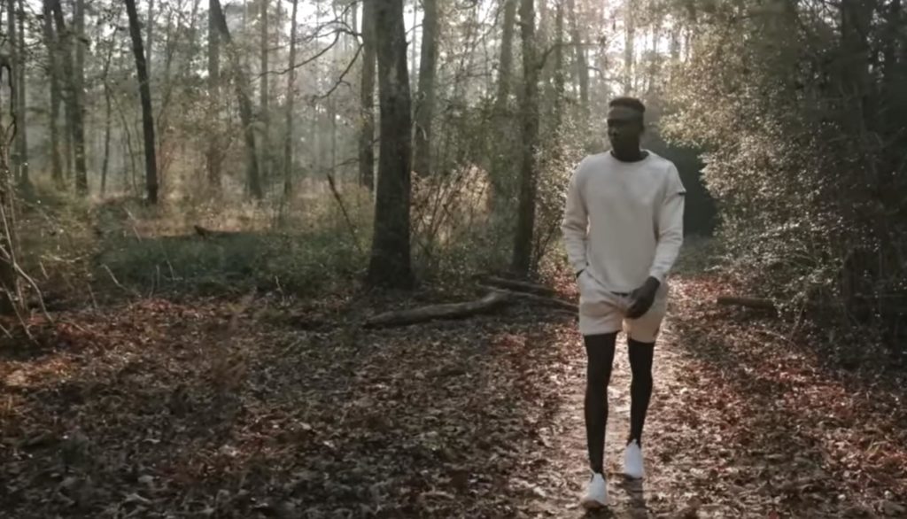 A man walks through a forest wearing Alphalete branded clothing