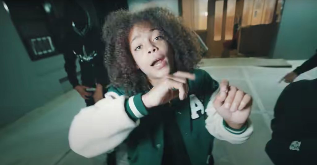 Drill artist SugarHill Ddot raps at the camera in a green and white baseball jacket