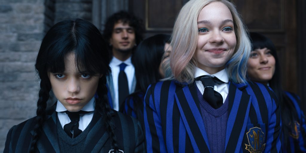 Jenna Ortega como Wednesday Addams y Emma Myers como Enid Sinclair frente a la Academia Nevermore vestidas de uniforme