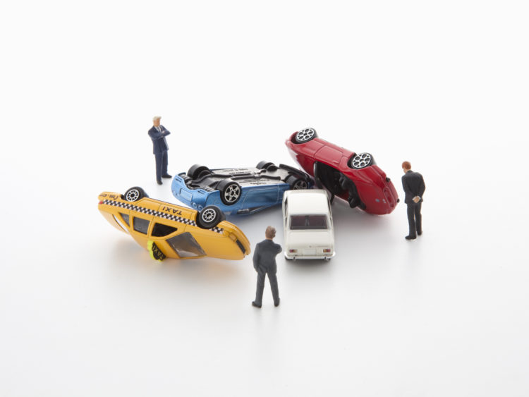 Toy cars piled in a mock wreck scenario, with three model drivers standing around