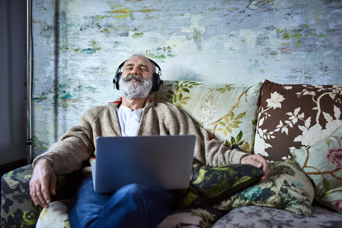Portrait of mature man on sofa smiling and wearing headphones