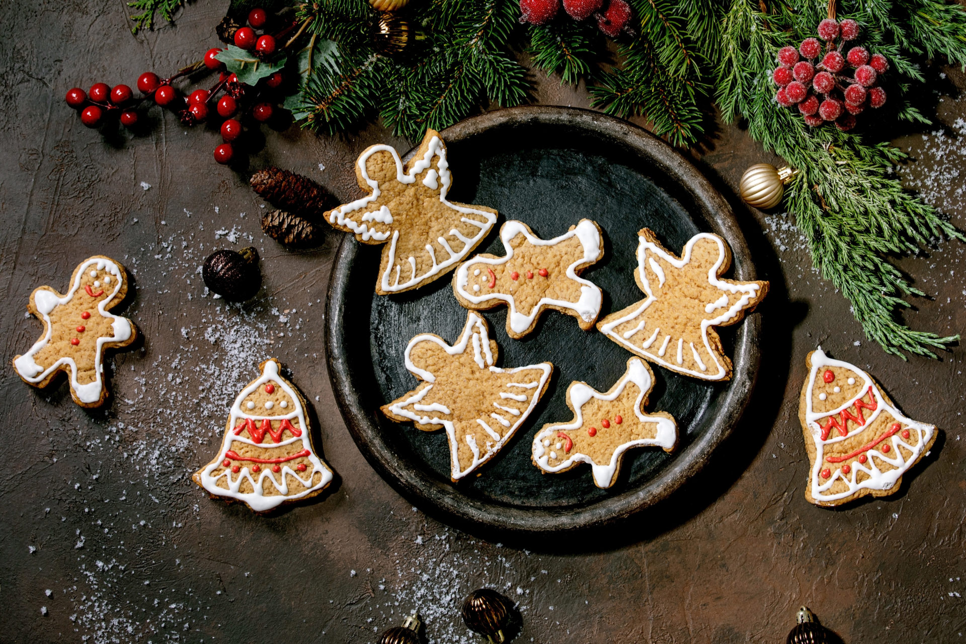 Homemade traditional Christmas gingerbread cookies with icing ornate. Gingerbread Man. angel. bell on ceramic plate with xmas decorations over dark background. Flat lay