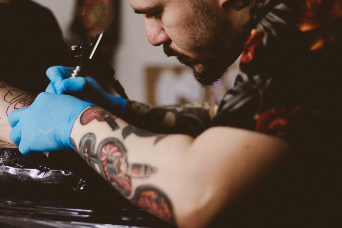Tattoo artist wearing blue gloves inks tattoo on client