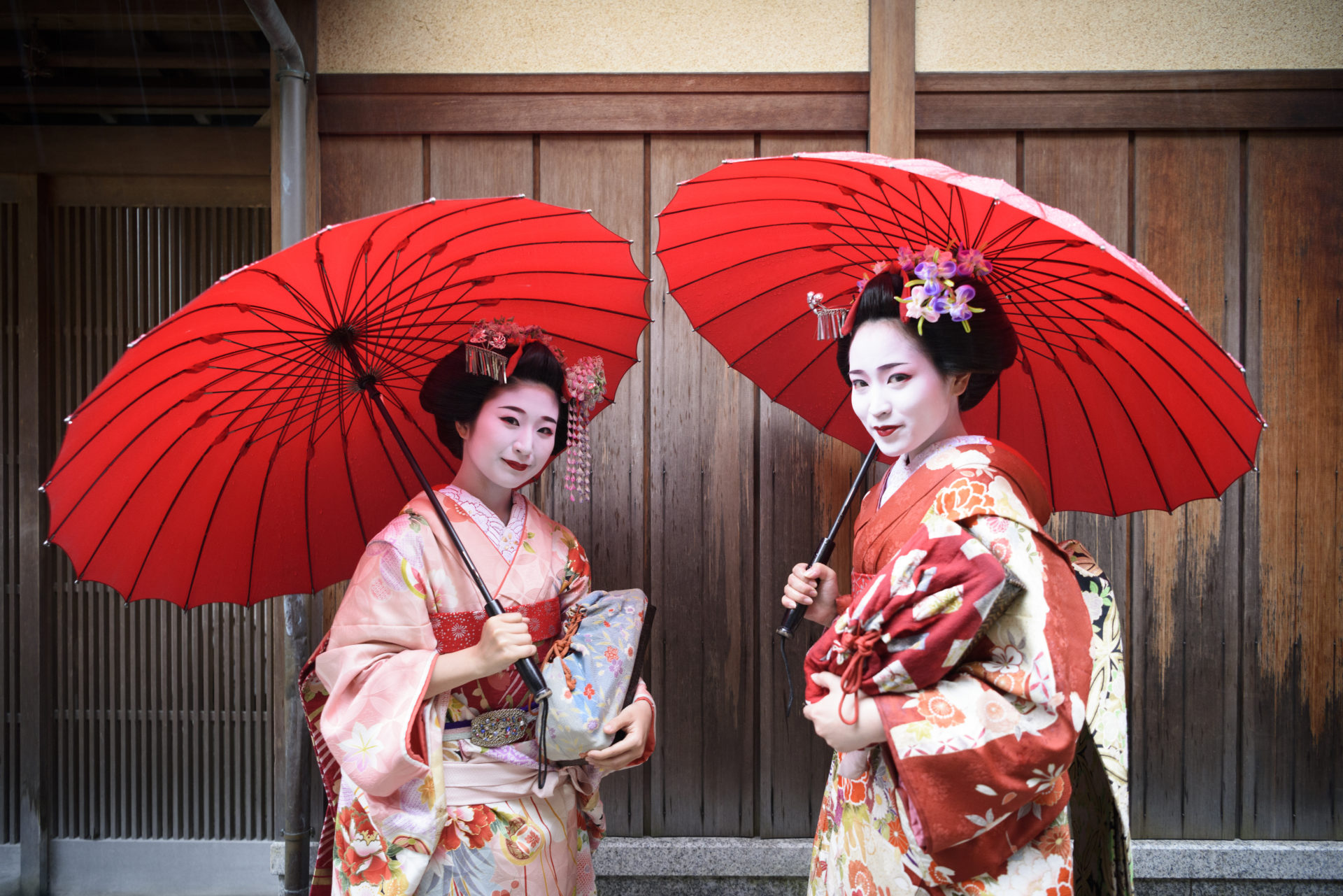 Two geisha girls wearing kimonos under red parasols