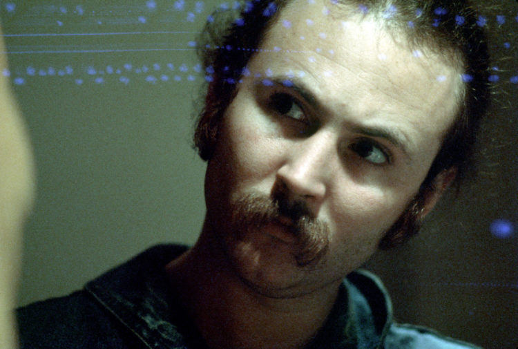 Old photo of David Crosby with his signature moustache, looking deep in thought