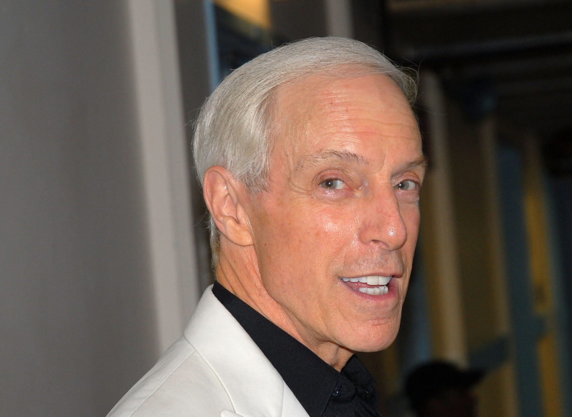 DJ Jerry Blavat in a black shirt and white suit jacket, smiling at the camera
