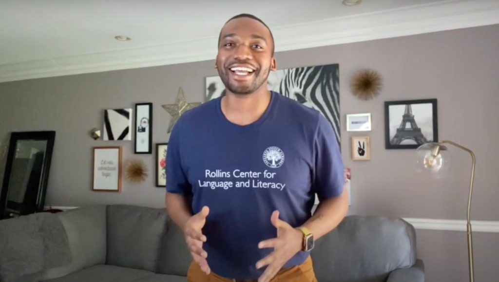 Quintin Bostic in a blue and purple t-shirt standing in the living room and teaching via digital learning