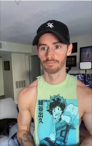 Dan Benson, wearing a cap and a vest top, stands in his living room, staring off into the distance (recording a TikTok video)